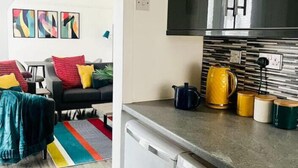 Ein kompakter Wohnbereich mit Küchenzeile, Waschmaschine und Essbereich mit Sofa und farbenfrohen Kissen.