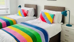 Ein Schlafzimmer mit zwei Betten, jedes mit einer bunten, gestreiften Decke und Kissen, einem Nachttisch mit einer Lampe und einem Bild an der Wand.