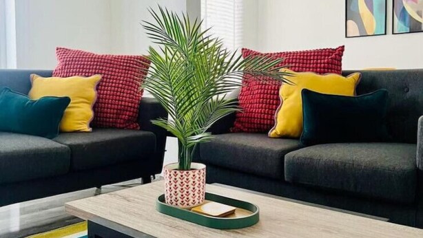 Ein modernes Wohnzimmer mit zwei dunklen Sofas, farbenfrohen Kissen, einem Holztisch und einem Streifenmuster-Teppich.