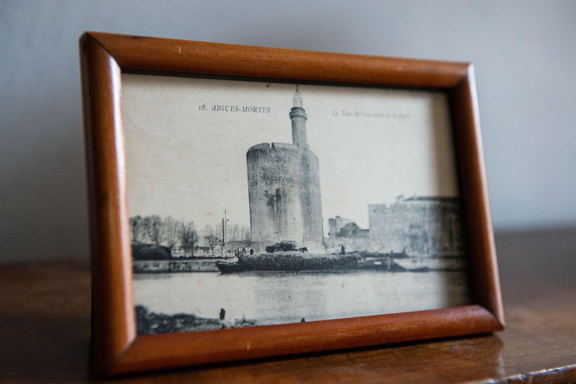 Une photographie en noir et blanc encadrée représentant un grand immeuble surmonté d’une flèche, avec la légende « AIGUES-MORTES ».