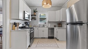A modern kitchen with white cabinets, stainless steel appliances, a hanging light fixture, and a patterned rug. - Downtown Retreat - Cozy Home Near Iconic Downtown (Fargo)