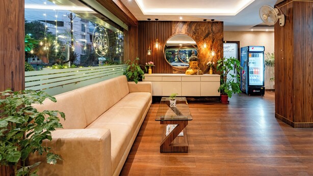 A modern reception area with a wooden reception desk, a sofa, and a large mirror. - Treebo Premium Zorba - Hoshangabad Road (Bhopal)