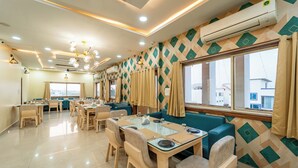 A hotel dining area with multiple tables and chairs, a large window with curtains, and a patterned wall design. - Treebo Premium Zorba - Hoshangabad Road (Bhopal)