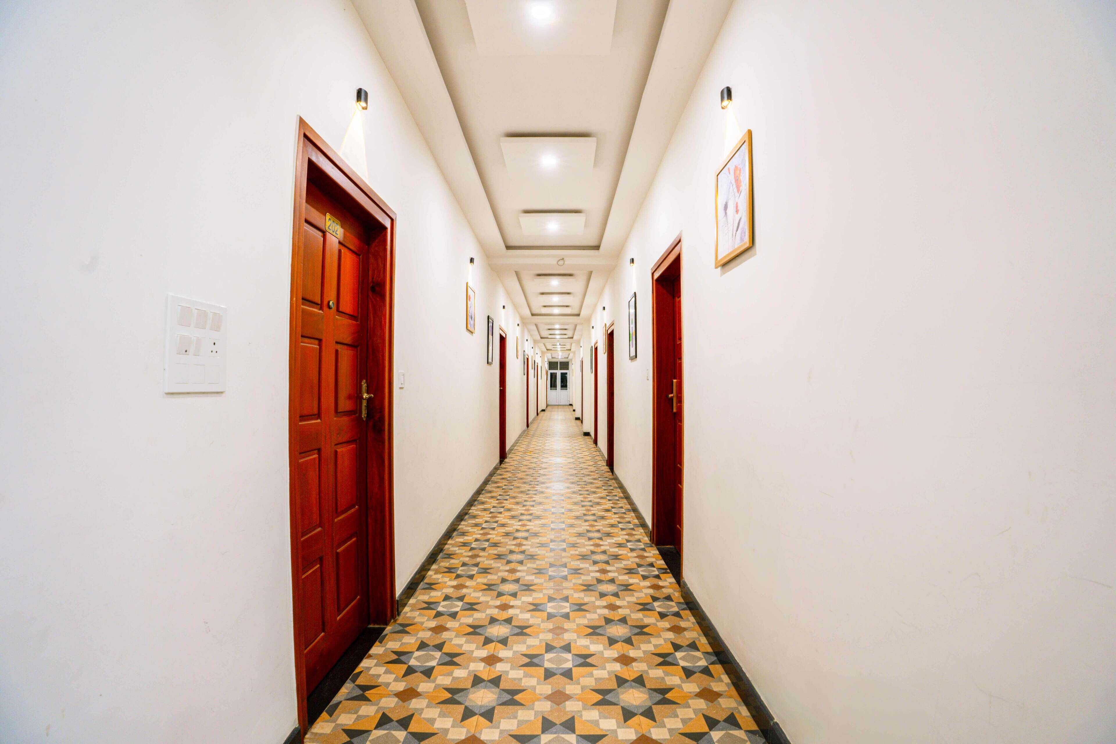 Un long couloir au sol décoré de motifs, avec des portes en bois et des tableaux encadrés accrochés aux murs.