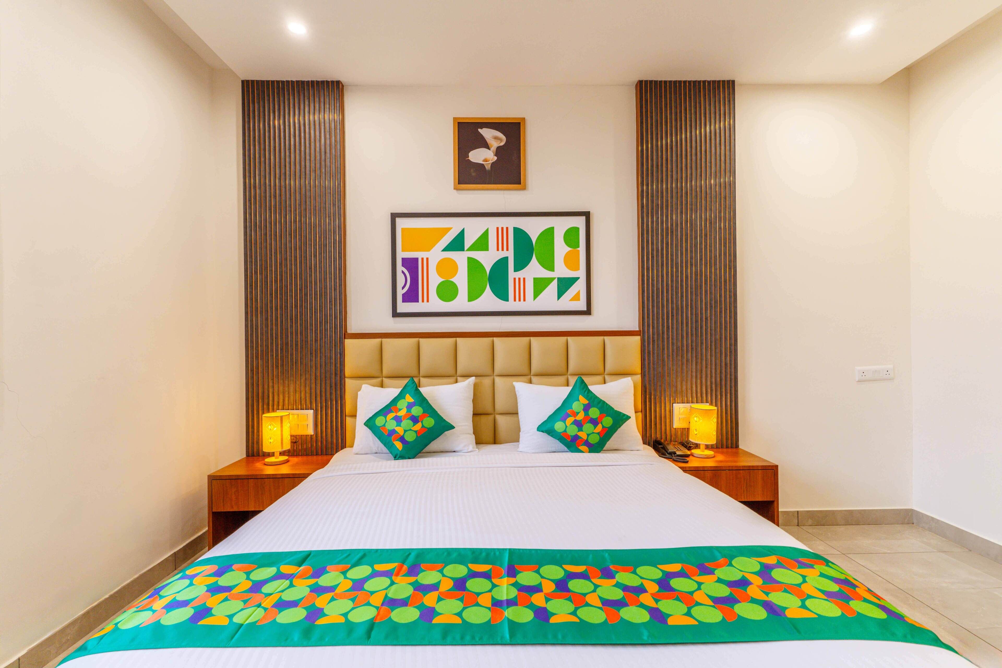 A hotel room with a large bed, two bedside tables with lamps, a headboard, and a framed abstract art piece above the bed.