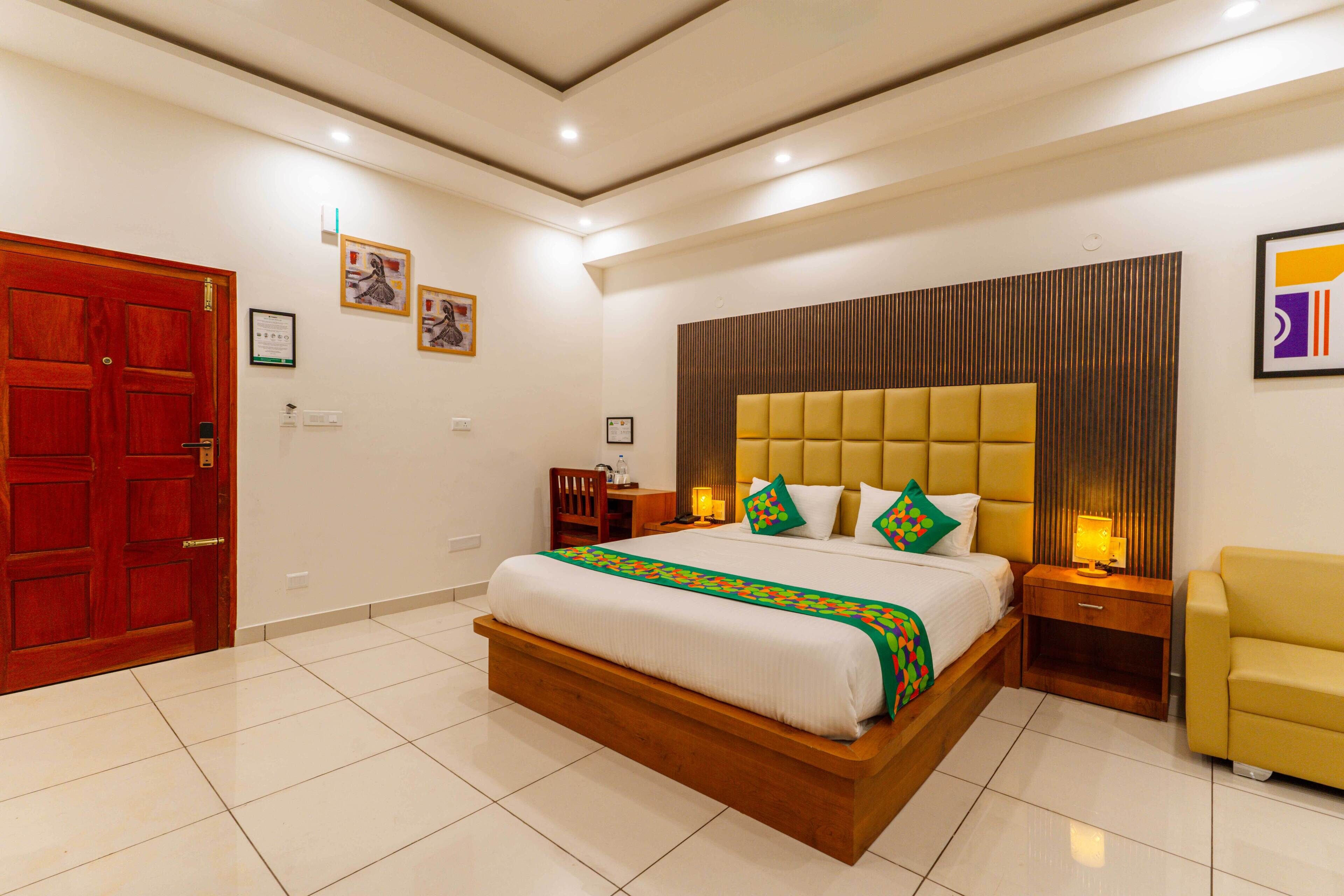 Una habitación de hotel con una cama grande, cabecera de madera, un sillón amarillo y una puerta roja.