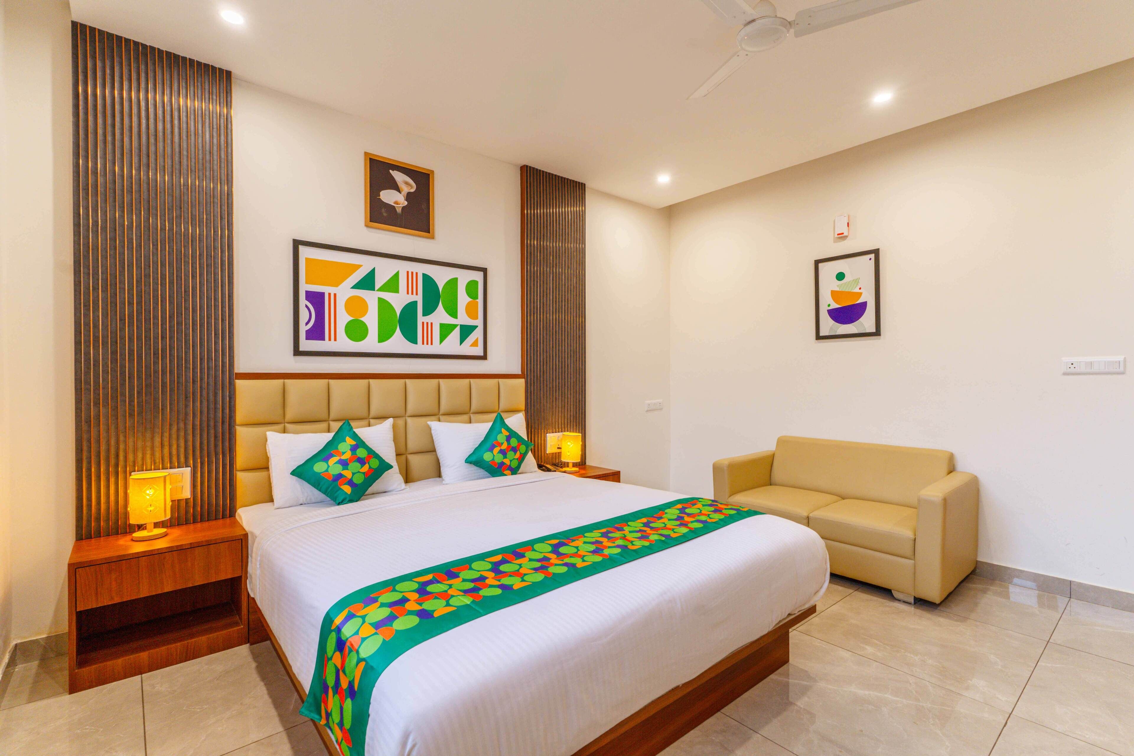 A hotel room with a large bed, two bedside tables with lamps, a sofa, and artwork on the walls.