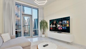 Ein modernes Wohnzimmer mit einem großen Flachbildfernseher, einer Couch, einem Couchtisch und Blick auf eine Stadtkulisse durch große Fenster.