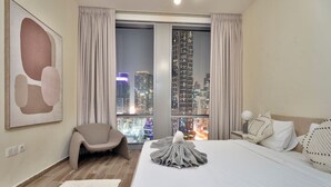 Ein modernes Hotelzimmer mit einem großen Bett, Blick auf die Stadt, einem Sessel und einem großen, abstrakten Gemälde an der Wand.