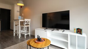 A modern living room with a flat-screen TV on a white stand, a wooden coffee table with a decorative plate, white chairs, and a white console table with a small statue and a colorful book. - w* | Bright 1BR in Historic Cusco w/ Balcony (Cusco)