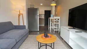 A modern living room with a grey sofa, a wooden coffee table, a TV, and a kitchen in the background. - w* | Bright 1BR in Historic Cusco w/ Balcony (Cusco)