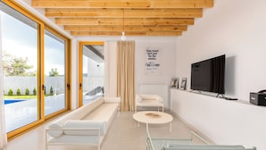 A modern living room with a large sliding glass door, a sofa, a coffee table, a TV, and a radiator. - 3BR Luxury Villa in Tbilisi (shindisi)