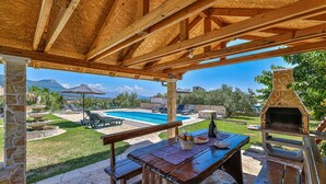 An outdoor patio with a pool, lounge chairs, a stone pillar, and a barbecue grill. - Exquisite Spacious Villa Bufaline With Pool and Gym (Kastela)