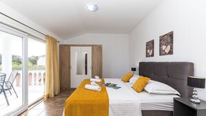 A bedroom with a bed, a nightstand, a chair, a balcony, and a door. - Exquisite Spacious Villa Bufaline With Pool and Gym (Kastela)