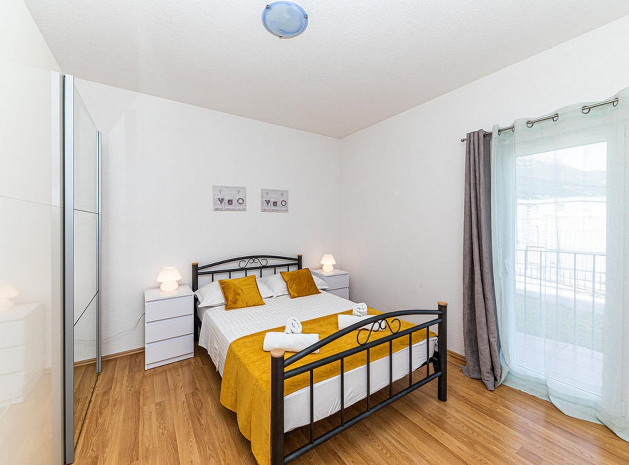 A bedroom with a bed, nightstands, a window with curtains, and a wall with two framed pictures.