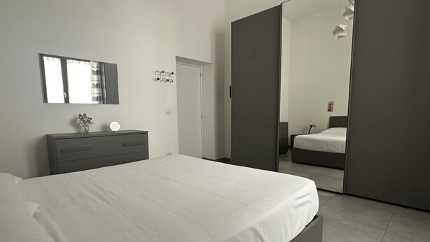 A modern bedroom with a large bed, a bedside table with a mirror, and a wardrobe.