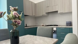 A modern kitchen with teal cabinets, a marble countertop, and a vase of flowers on a table.