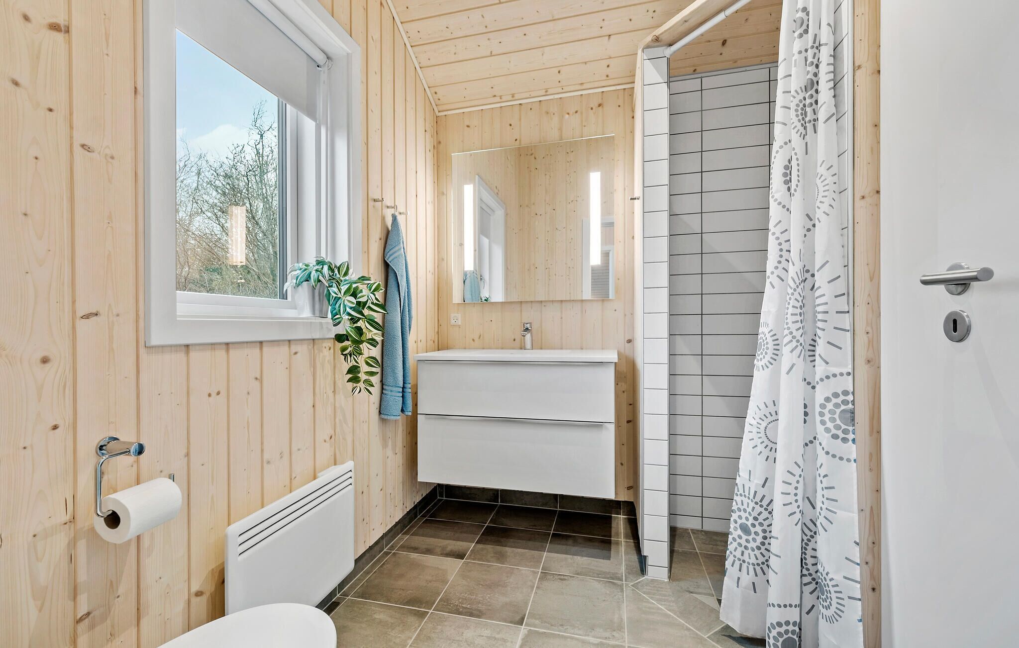 A bathroom with wooden walls, a window, a sink, a mirror, a towel, a toilet, and a shower curtain.