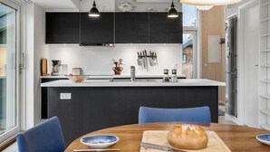 A modern kitchen with a central island, black cabinets, and a dining area with blue chairs. - 2 bedroom gorgeous home in Kalundborg (Kalundborg)