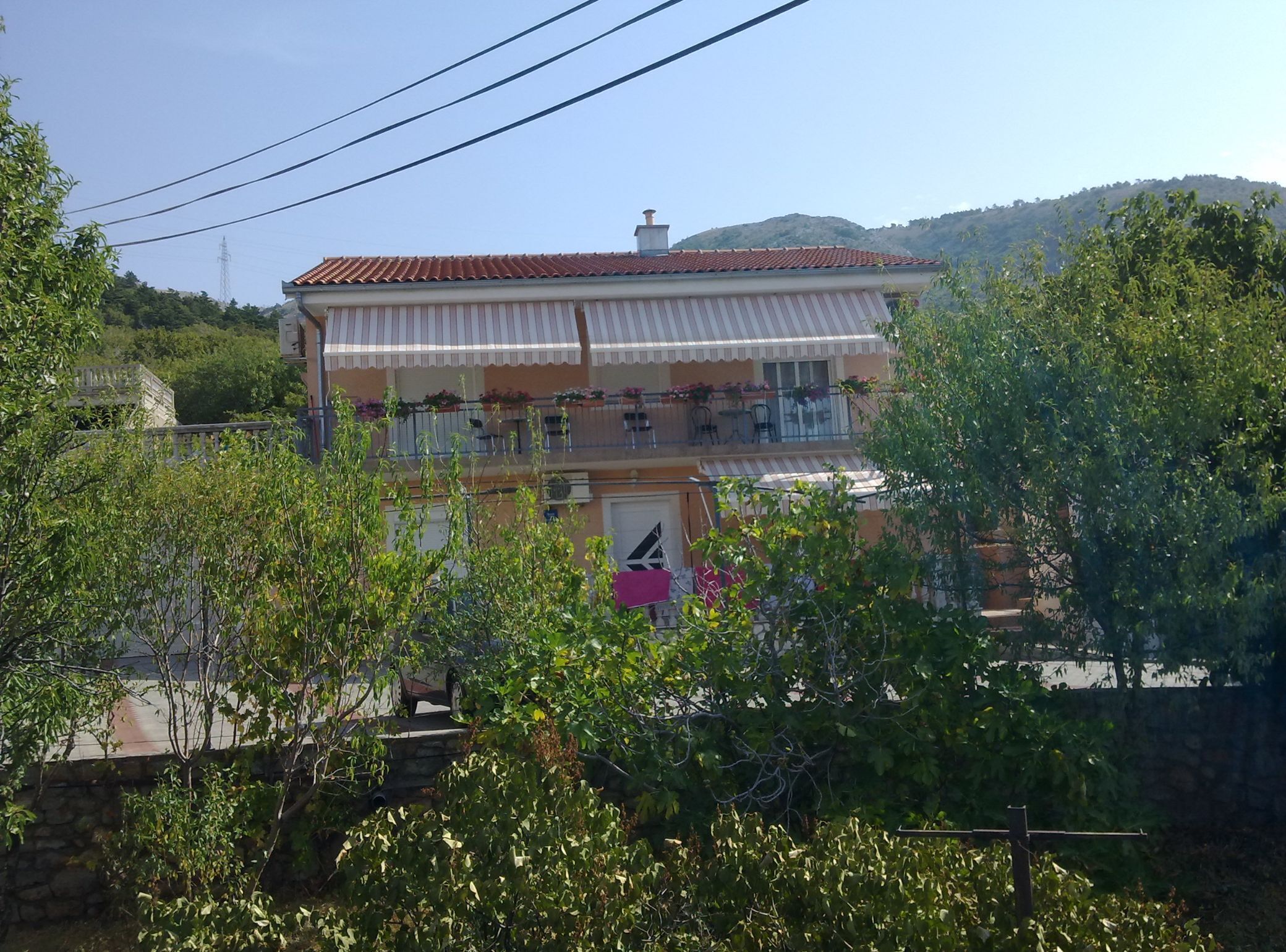 A two-story building with a red-tiled roof and a balcony with outdoor seating.