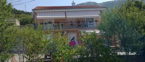 A two-story building with a red-tiled roof and a balcony with outdoor seating.