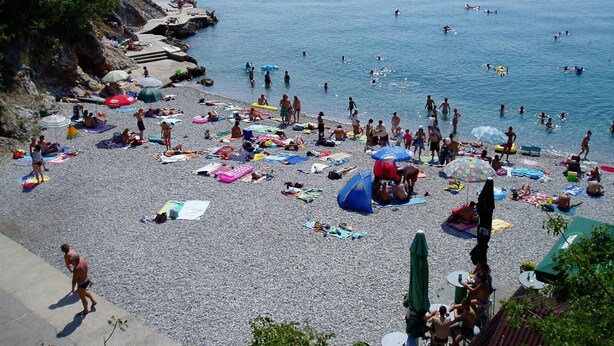 Een druk strand met mensen die zonnebaden en zwemmen.