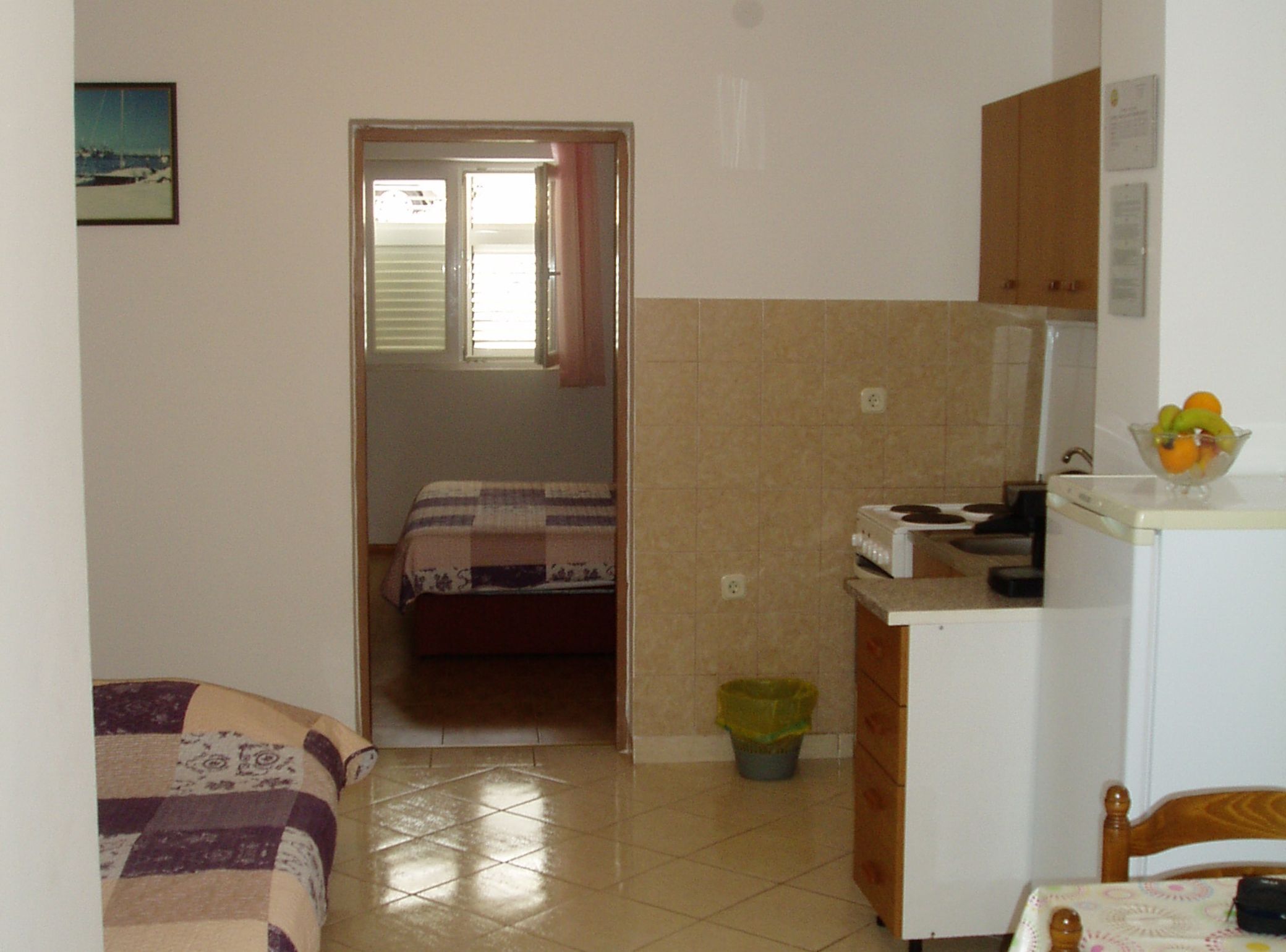 Una habitación pequeña y compacta con una cama, un rincón americano y una puerta que da a otra habitación.