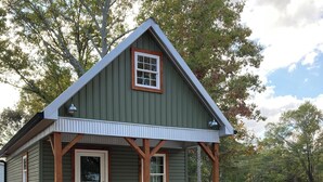 A small, single-story house with a green exterior and a white door, surrounded by a wooden deck and a mulched garden area. - Broyles Landing Cottage at Lake Hartwell SC (Townville)