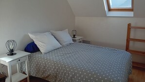 Un dormitorio con cama, mesita de noche, escritorio, ventana y vistas a montañas, además de una escalera de madera.