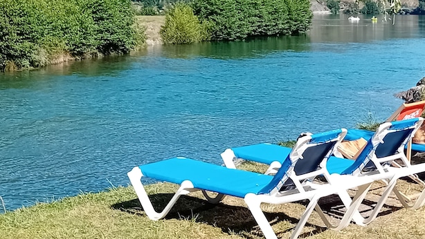 Vista al río con sillas reclinables azules y una zona con césped.