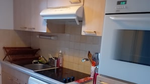 Cocina equipada con lavavajillas, estufa y horno. Se observa un escurreplatos de madera y un portaobjetos.