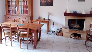 Un comedor con una mesa y sillas de madera, un mueble de madera con puertas de cristal, un cuadro en la pared y una chimenea con leña.