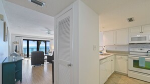 Una cocina moderna con armarios blancos, un microondas y una estufa. Hay un comedor con mesa y sillas, y una vista al océano a través de amplias ventanas.