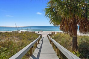 A wooden boardwalk leading to a beach with a palm tree and a clear blue sky.