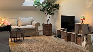 Una sala de estar con sofá, mesa de centro, mueble para televisión, lámpara, planta y tragaluz.