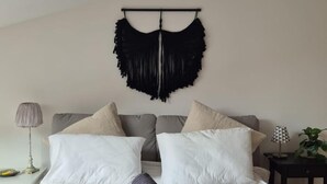 Un dormitorio con cama, almohadas, una colcha, un adorno en la pared, una lámpara y una mesita con una planta.
