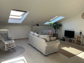 Ein Wohnzimmer mit einer Couch, einem Schaukelstuhl, einem Fernseher und einer Pflanze.