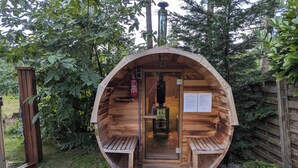 Estructura de sauna de madera con bancos en su interior, rodeada de vegetación.