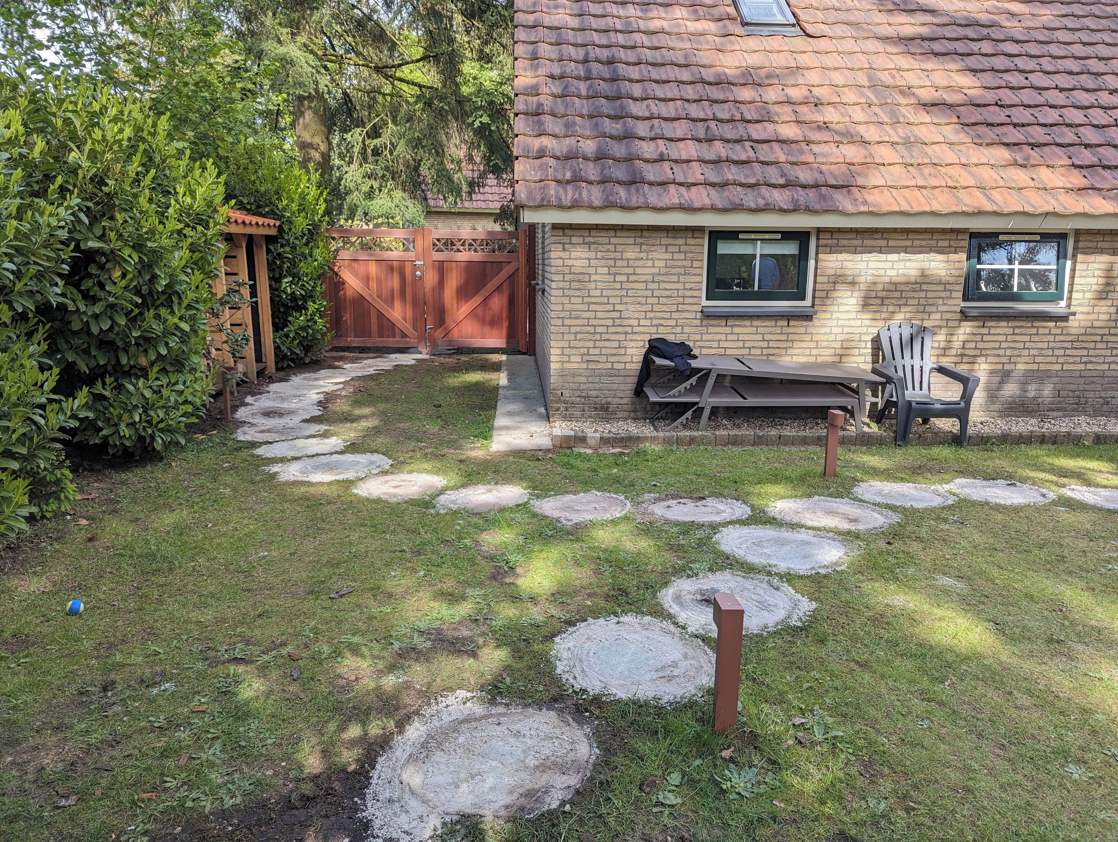 Een huis met een bakstenen gevel, een houten terras en een pad van stenen dat naar de voordeur leidt.