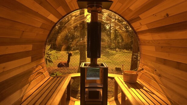 Una cabaña de madera con un ventanal circular, chimenea y terraza de madera.