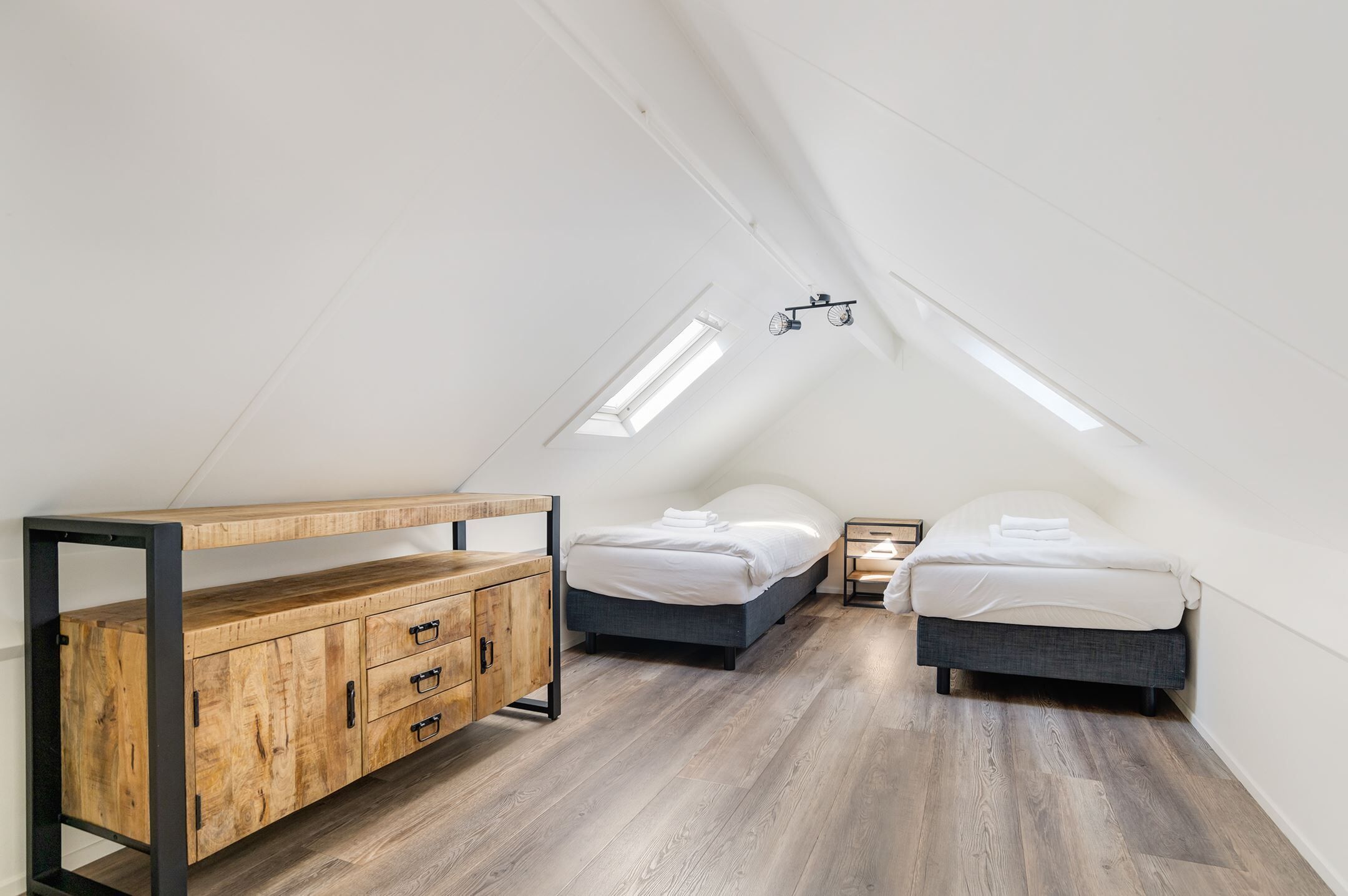 A loft bedroom with a sloped ceiling, two beds, a wooden dresser, and a skylight.