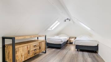 A loft bedroom with a sloped ceiling, two beds, a wooden dresser, and a skylight.