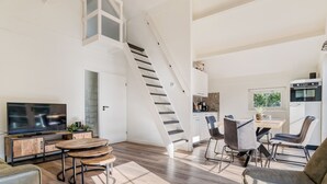Una sala moderna con televisor, muebles de madera, una escalera y una zona de cocina.