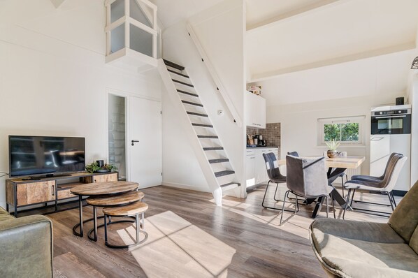 A modern living room with a TV, wooden furniture, a staircase, and a kitchen area.
