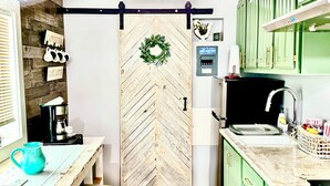 A kitchen with a herringbone wood pattern wall, a coffee machine, a sink, and green cabinets. - Peaceful Charming Tiny Home (Kyle)