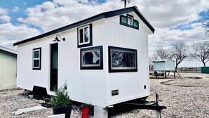 A small, white mobile home with a black roof, multiple windows, and a small porch area. - Peaceful Charming Tiny Home (Kyle)