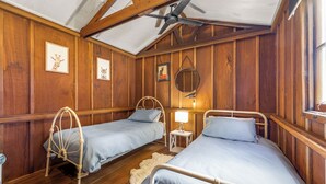 Ein Zimmer mit zwei Betten, Holzwänden, einem Deckenventilator und gerahmten Bildern an der Wand.