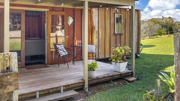 Eine Holzterrasse mit Sitzgelegenheiten im Freien, einer Tür zum Innenbereich und einem kleinen Tisch mit einem Blumentopf.
