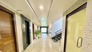 Un couloir d’hôtel moderne avec un sol en marbre, des portes en bois et en verre, un escalier et une plante en pot.