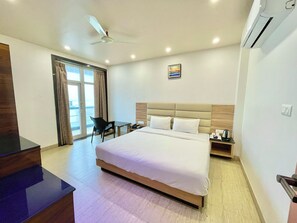 Une chambre d’hôtel avec un grand lit, un bureau, une chaise, un ventilateur de plafond et une vue par la fenêtre.